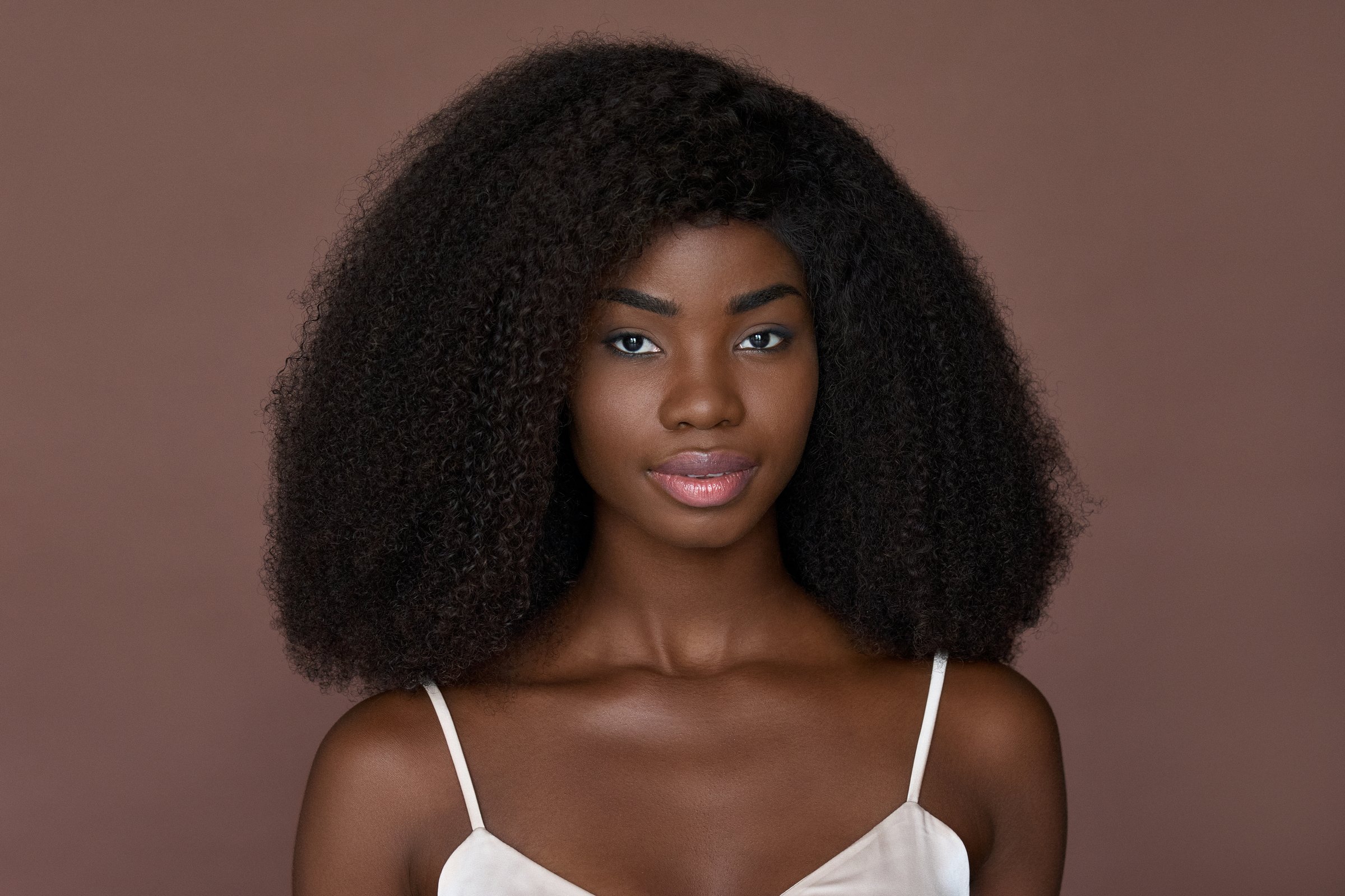 Portrait of a woman with natural hair against a warm brown background
