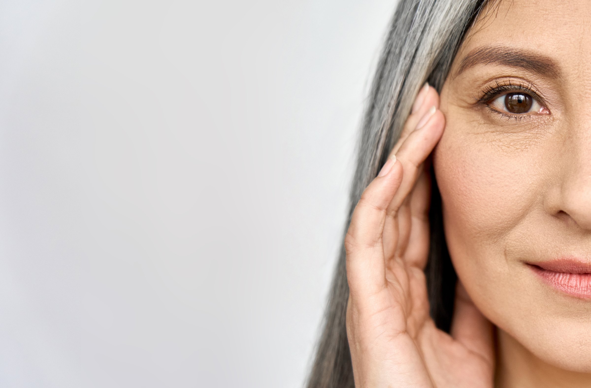 Half-face close-up of a silver-haired woman, hand raised to her cheek