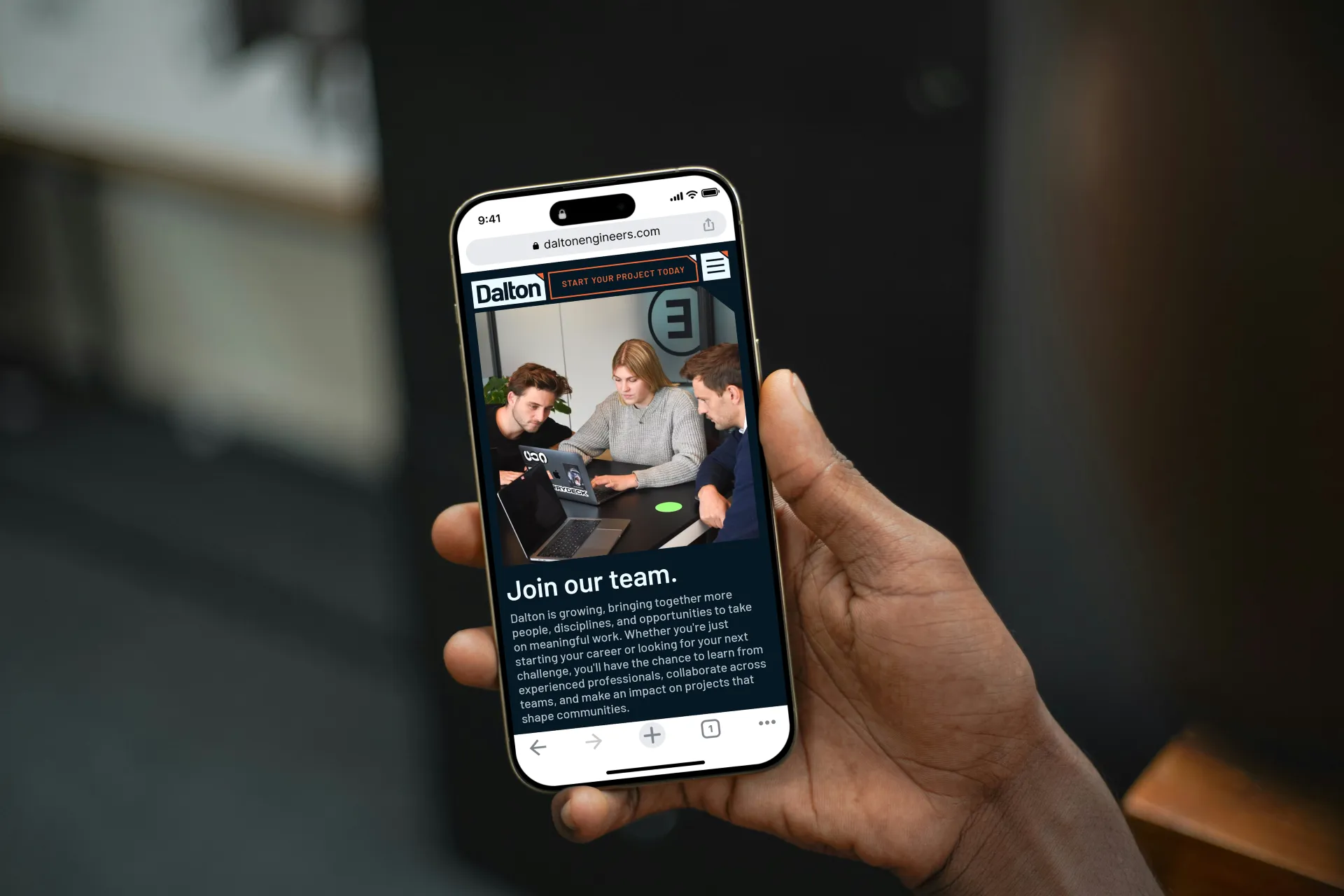Hand holding a smartphone showing the Dalton Engineers careers webpage with three people collaborating over laptops and text inviting to join the team.