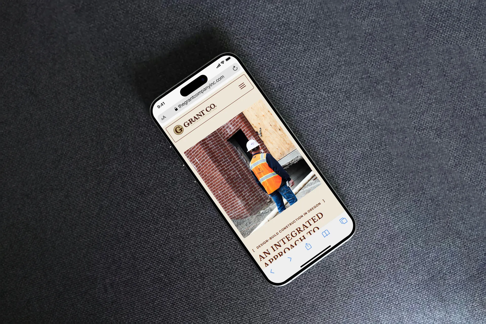 Mobile phone laying on table with screen open to The Grant Company website showing construction worker.