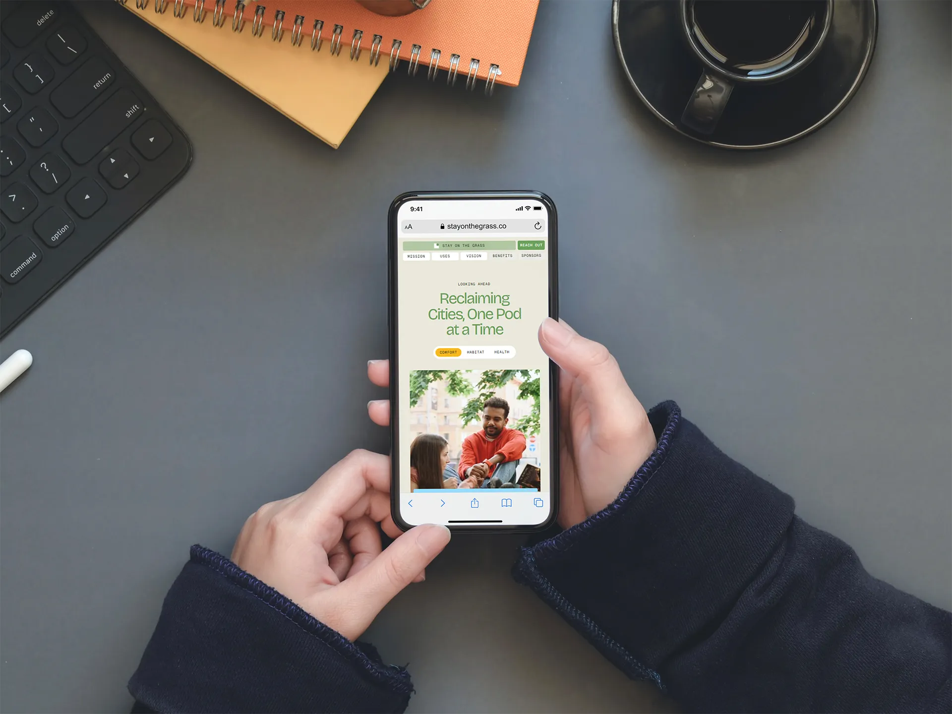Image of person holding a phone on their desk, Stay on the Grass website on the phone screen.