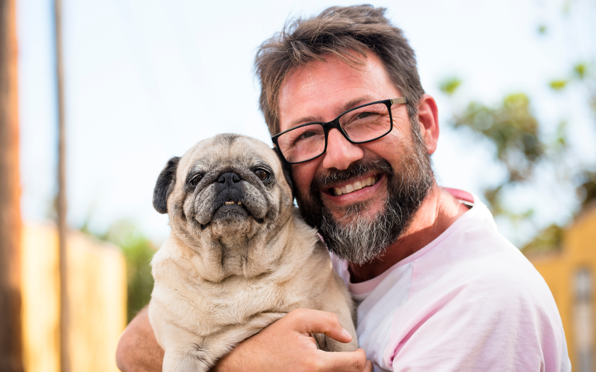 Smiling man wearing glasses holding his pug