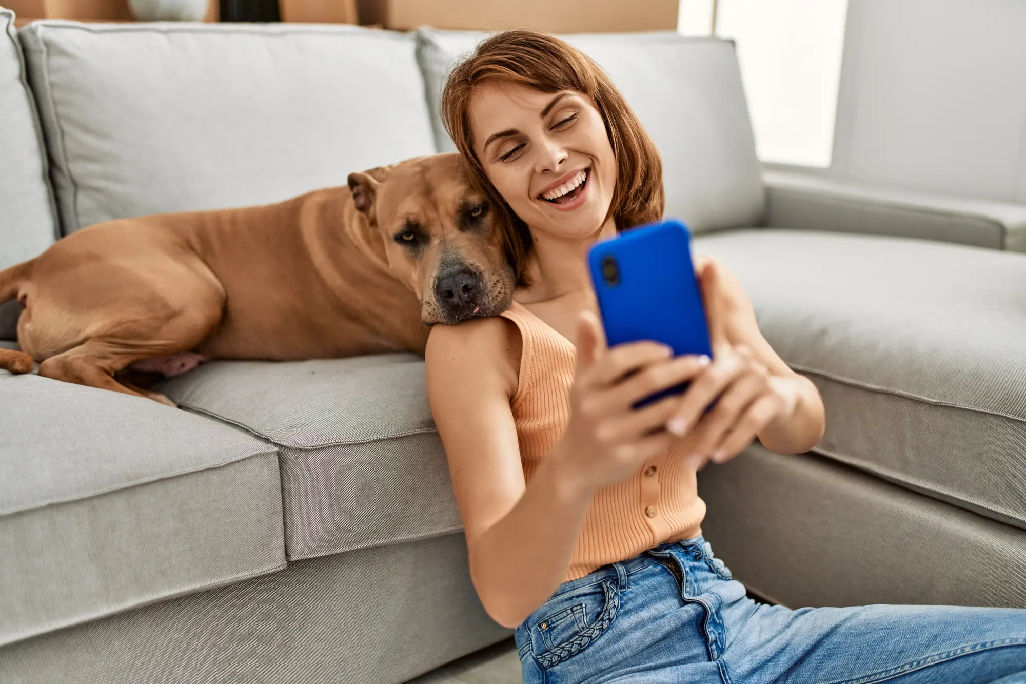Woman smiling and holding her small dog while looking at her phone at home