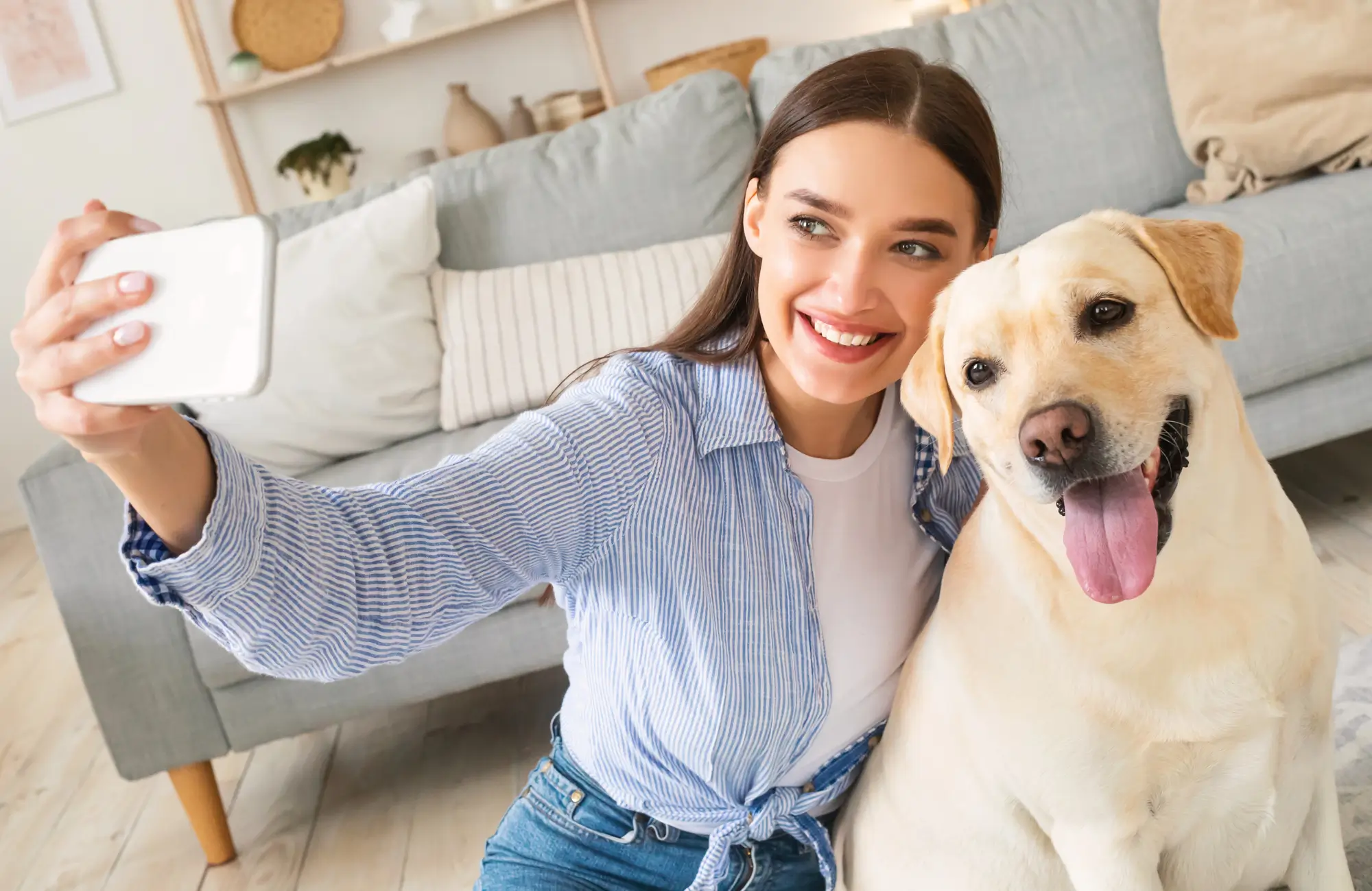 Woman smiling and holding her small dog while looking at her phone at home