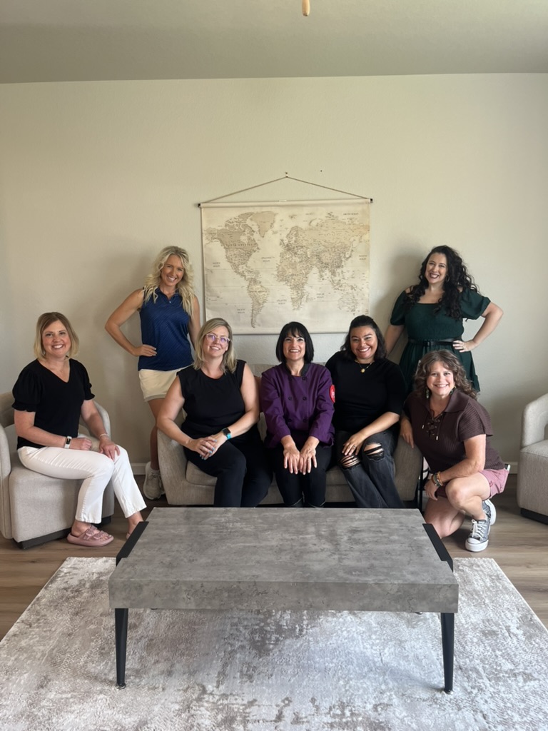 Plandipity Doers team photo: seven women posing together in modern living room with world map