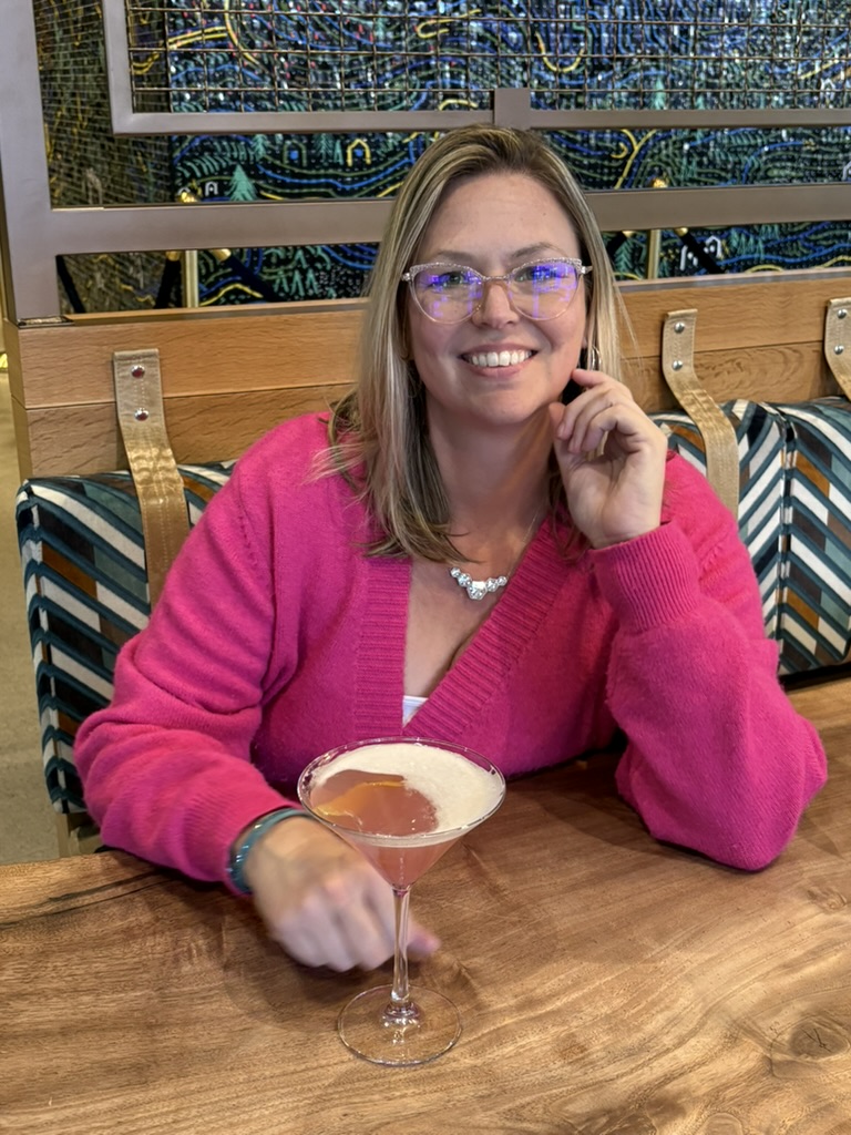 Samantha Markey smiling in pink cardigan with cocktail at restaurant table