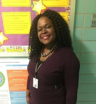 Dr. Louissaint smiling in front of classroom bulletin board
