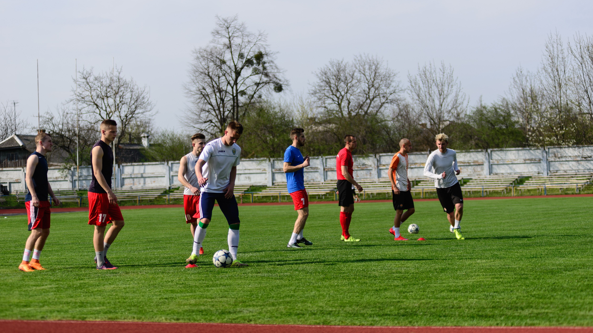 Soccer players participating in a training drill with soccer balls on an outdoor field.