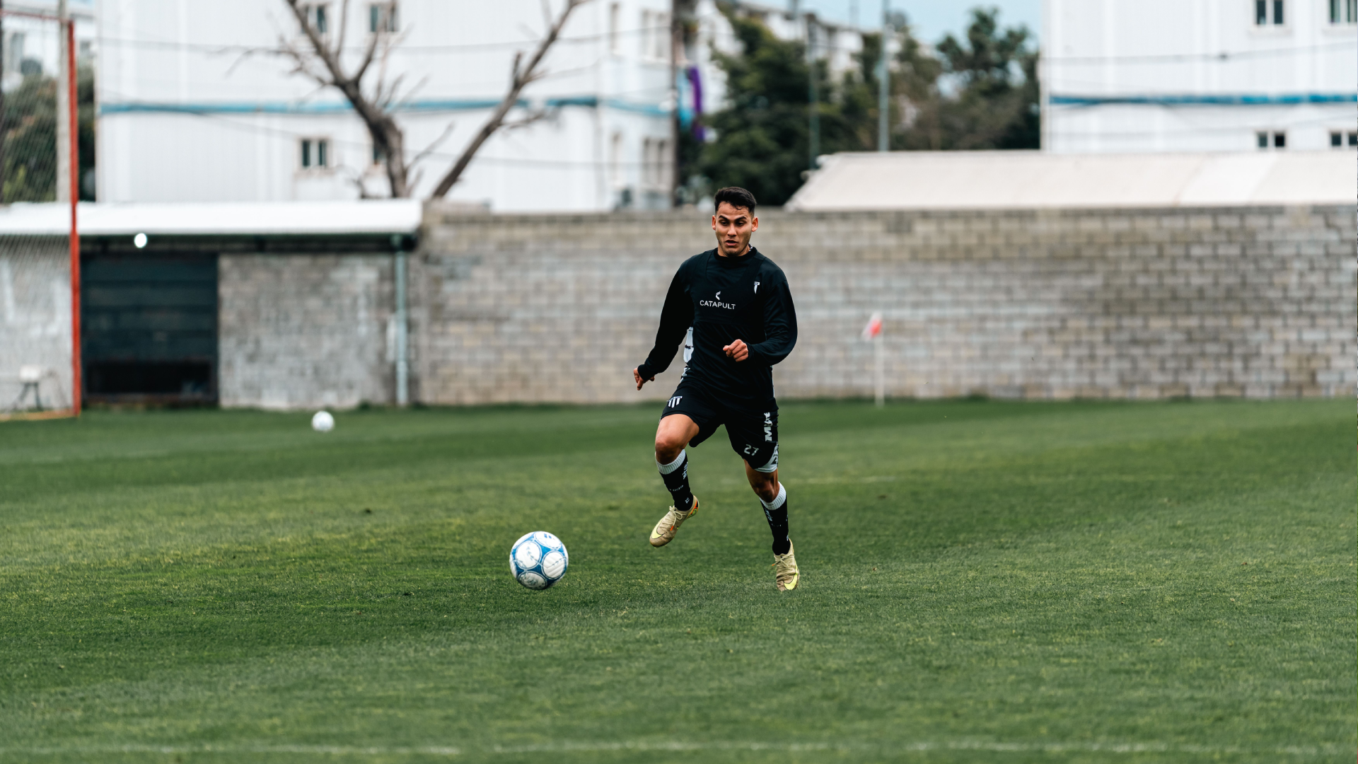 Soccer player running toward the ball during a training session on an outdoor grass field.