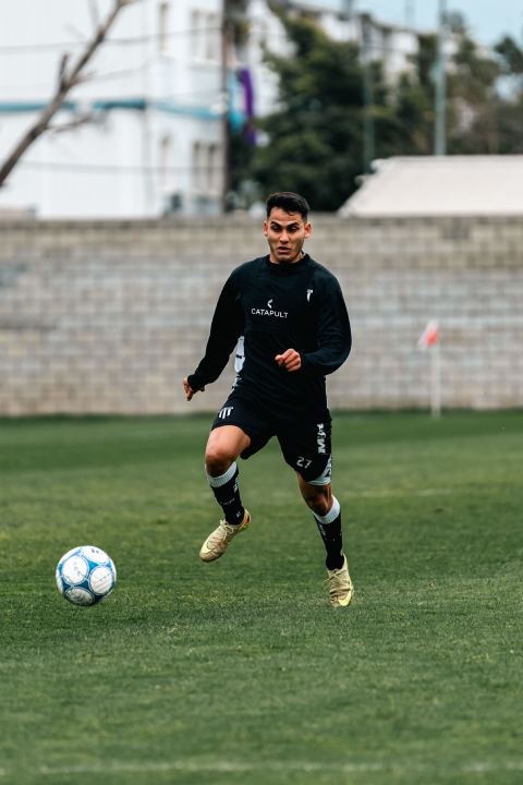 Soccer player running toward the ball during a training session on an outdoor grass field.
