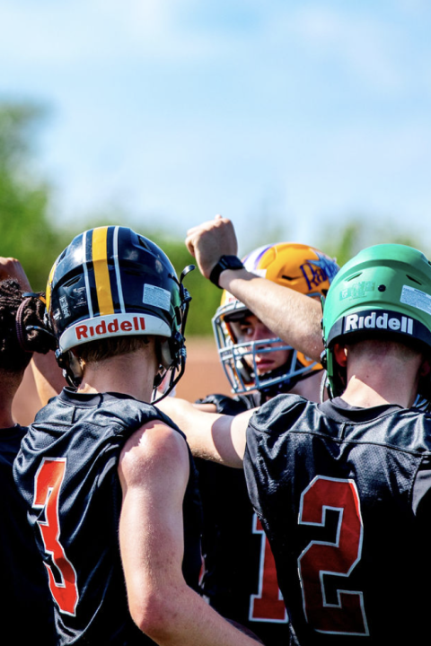 Youth football team huddled together with arms raised in a team spirit gesture on the field.
