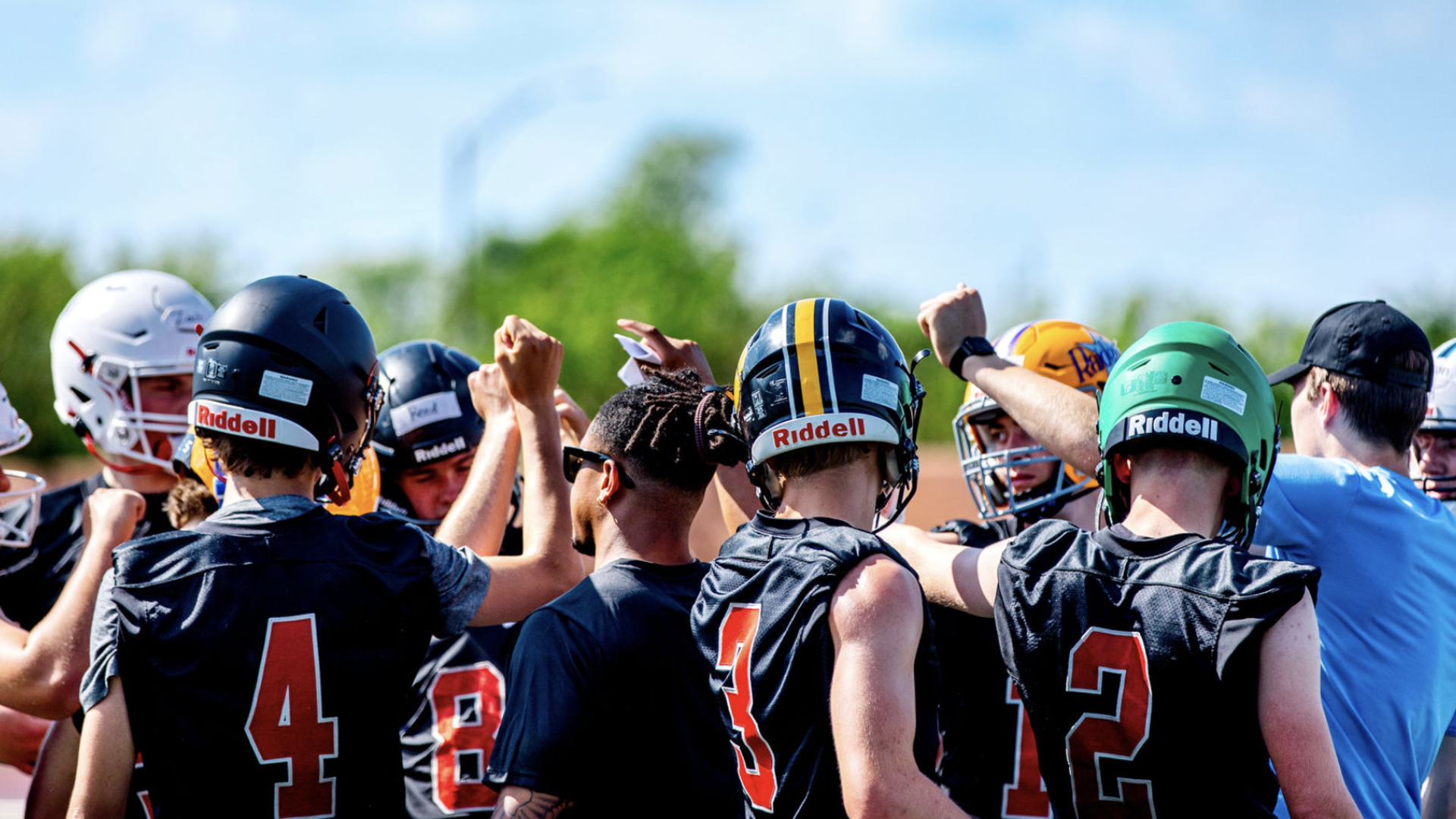 Youth football team huddled together with arms raised in a team spirit gesture on the field.