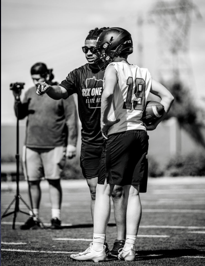 Football coach giving instructions to a young quarterback during an outdoor training session.