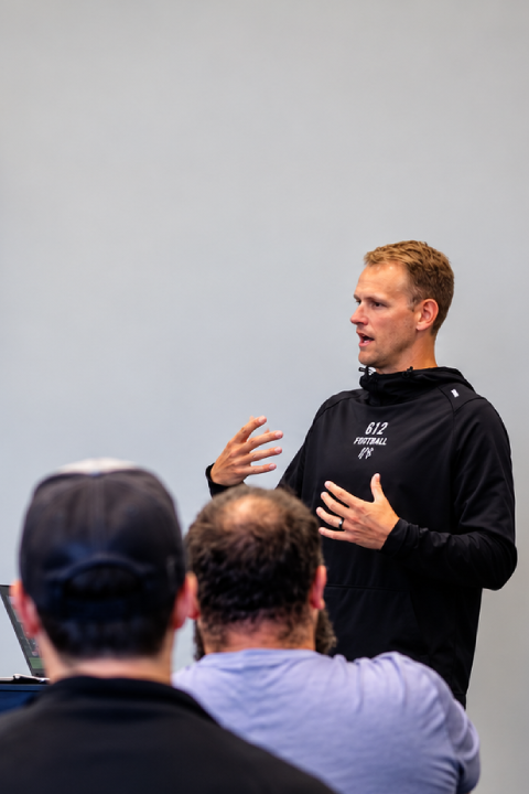 612 Football coach presenting to families at the Summer Youth Camp, focused on the coach rather than the background screen.