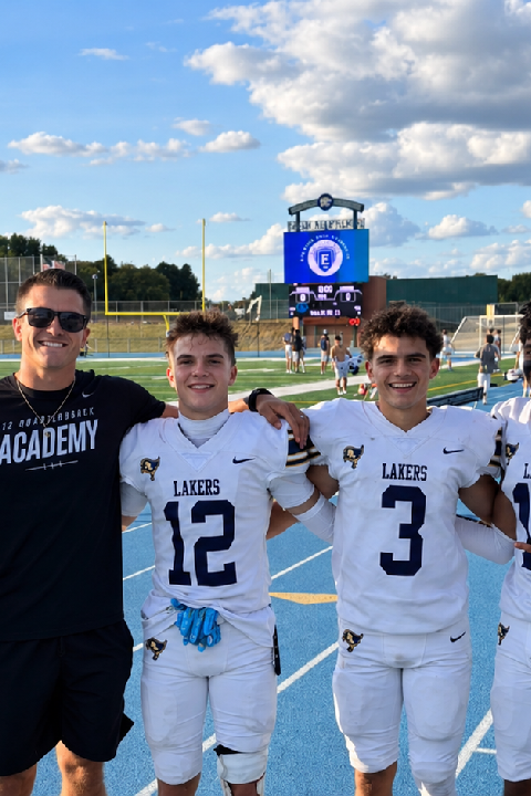 Football coach posing with five high school players in uniform on a football field after a game.