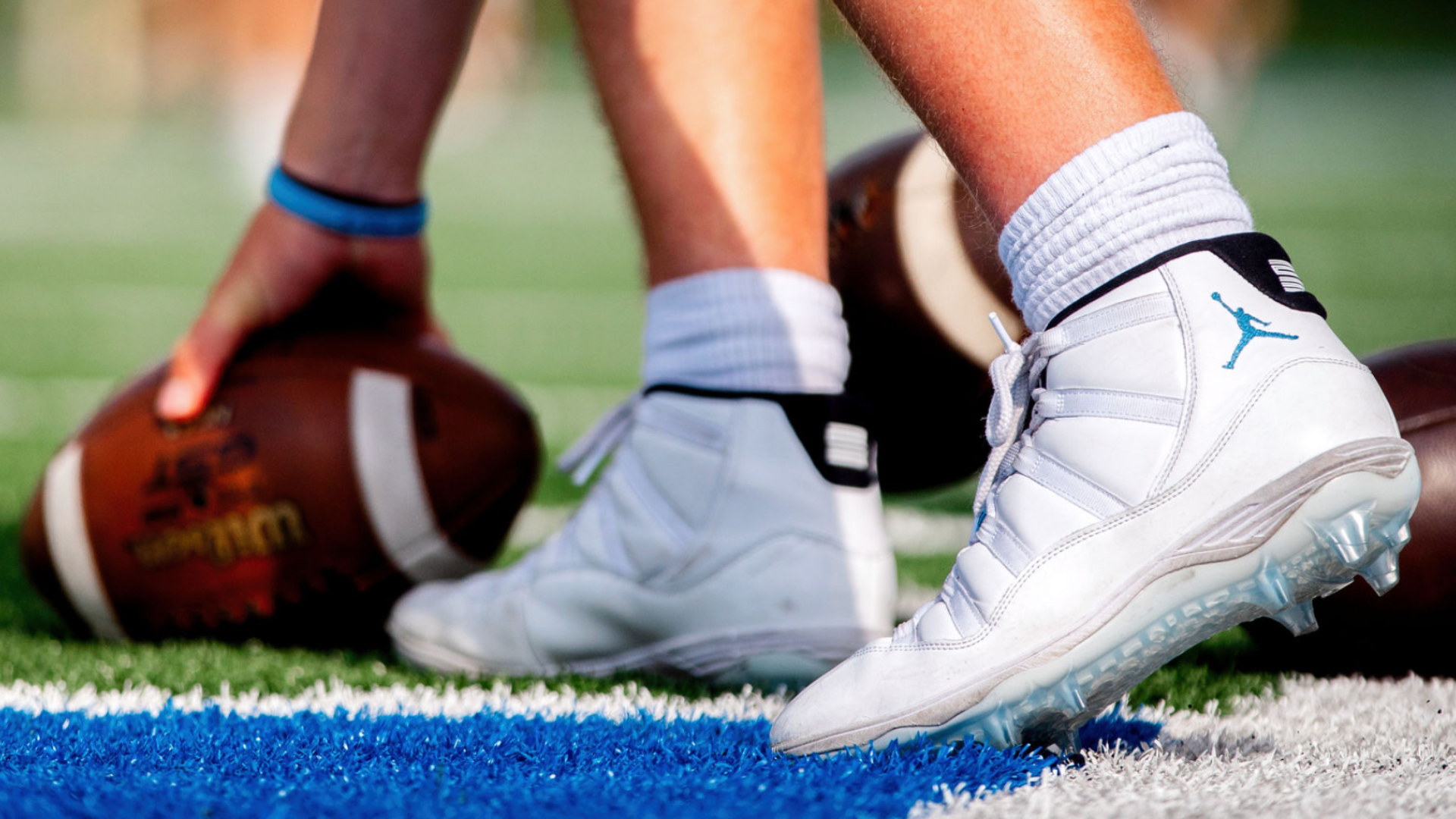 Close-up of a football player in white cleats preparing with a football on an outdoor turf field.