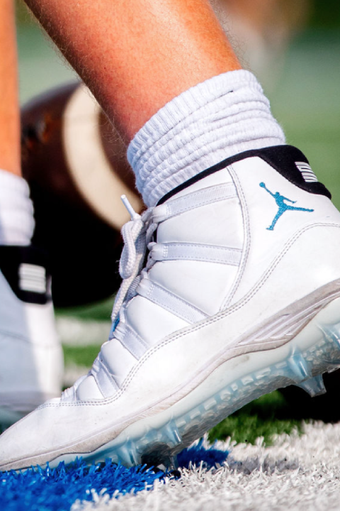 Close-up of a football player in white cleats preparing with a football on an outdoor turf field.