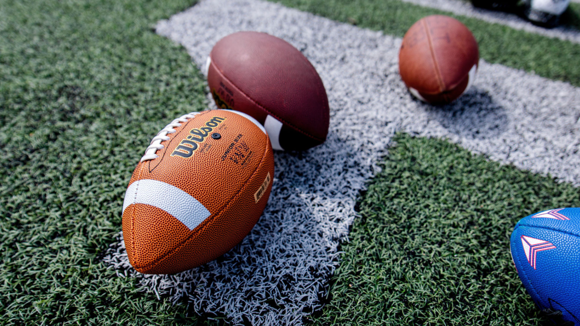 Football training balls arranged on artificial turf along a white field line.