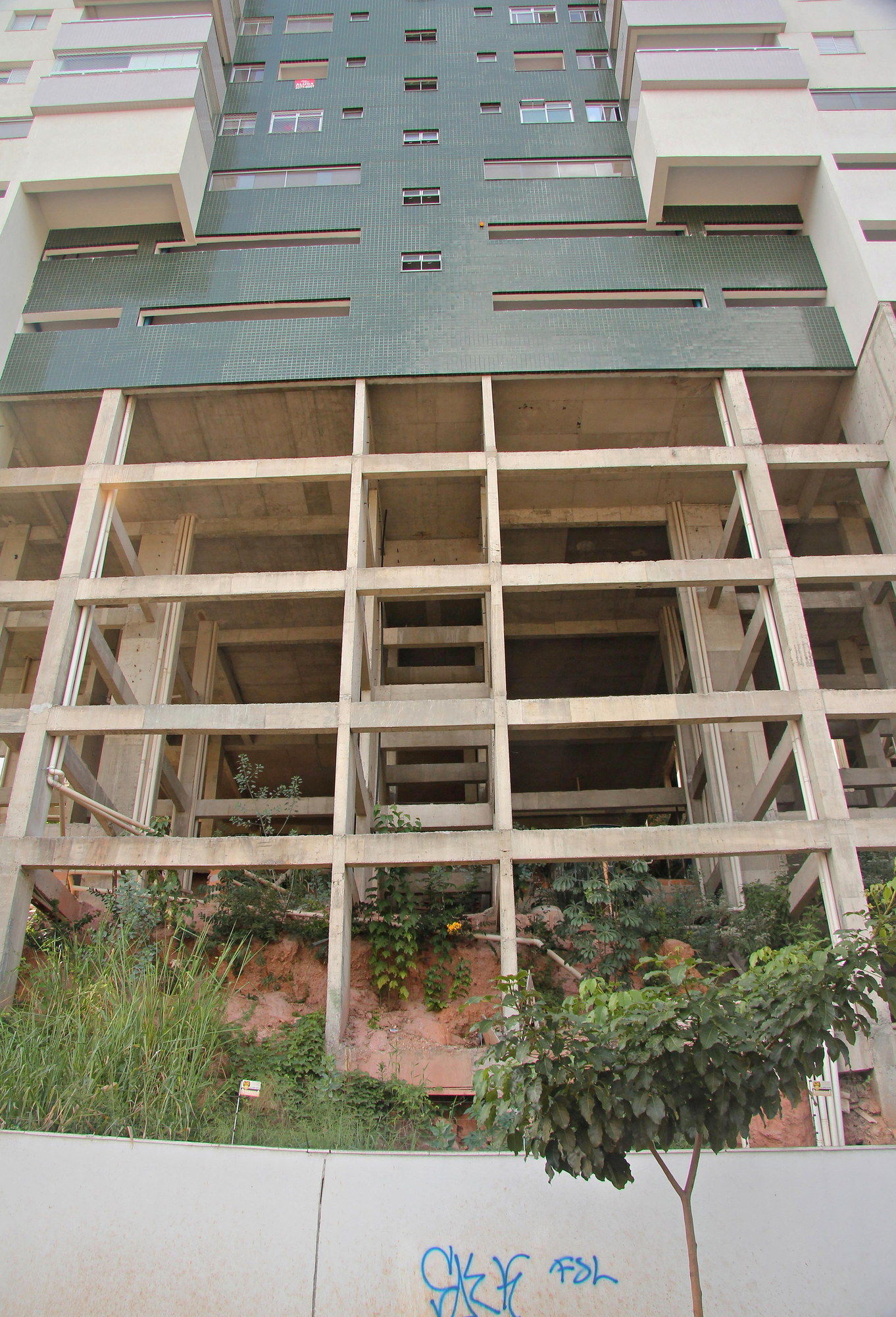 Looking up at the palafita from the street in 2018: a residential tower standing on a concrete frame roughly six storeys tall, weeds and bare earth beneath it