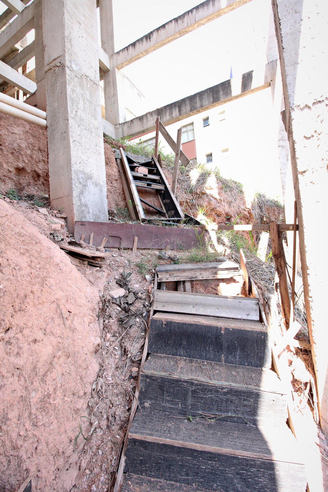 The improvised timber stair down the cut beside the building, between the retaining wall and the razor wire
