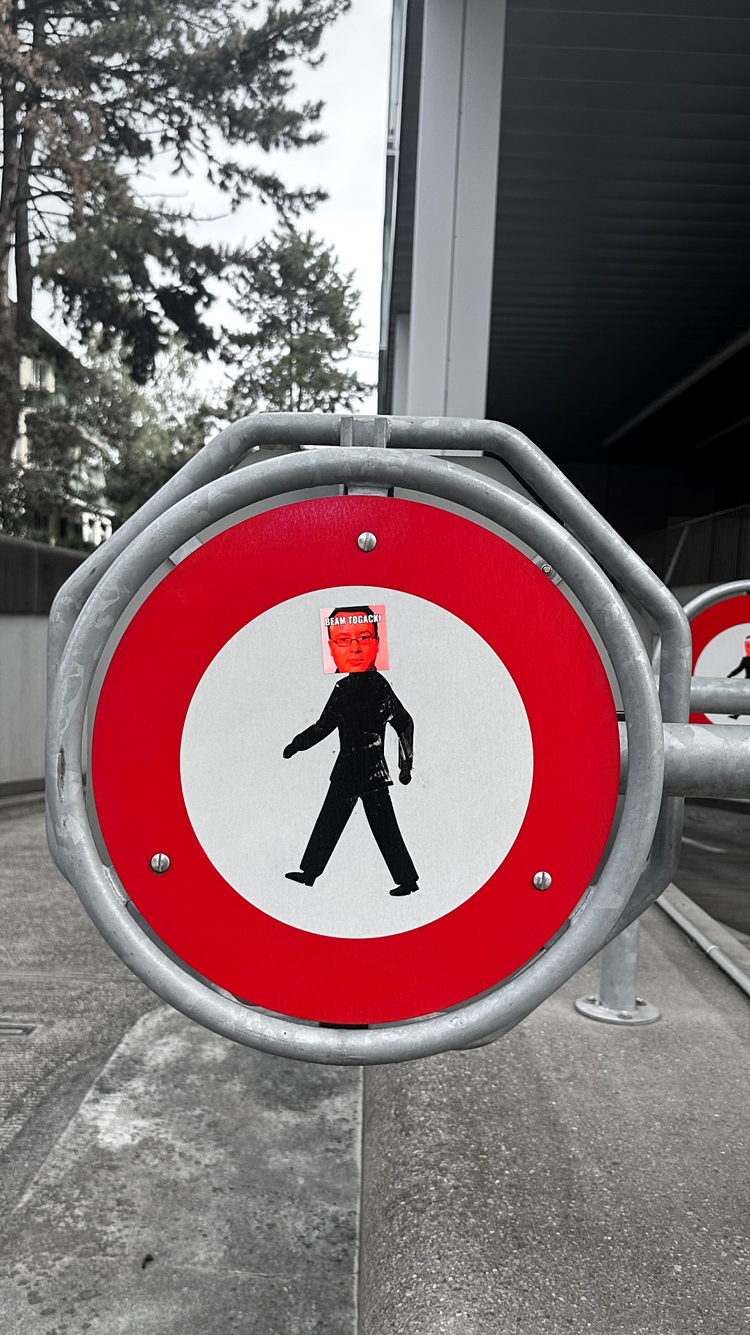 The other kind of intervention: on a round no-pedestrians sign, somebody covered the walking man's head with a printed sticker of a face — no drawing, no joke in the sign's language