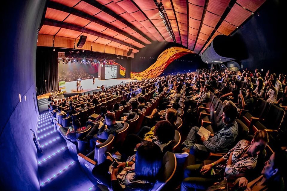 CX Experience · 2019 — A full auditorium under a red slatted ceiling.