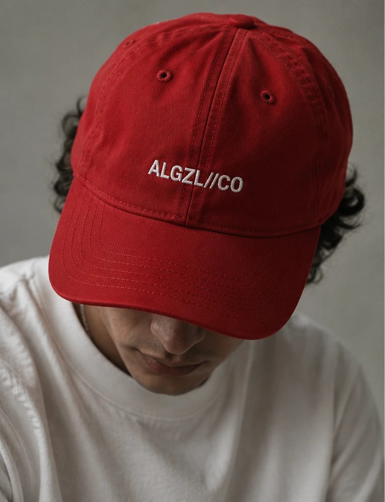 The cap — red cap with ALGZL//CO embroidered in white, worn
