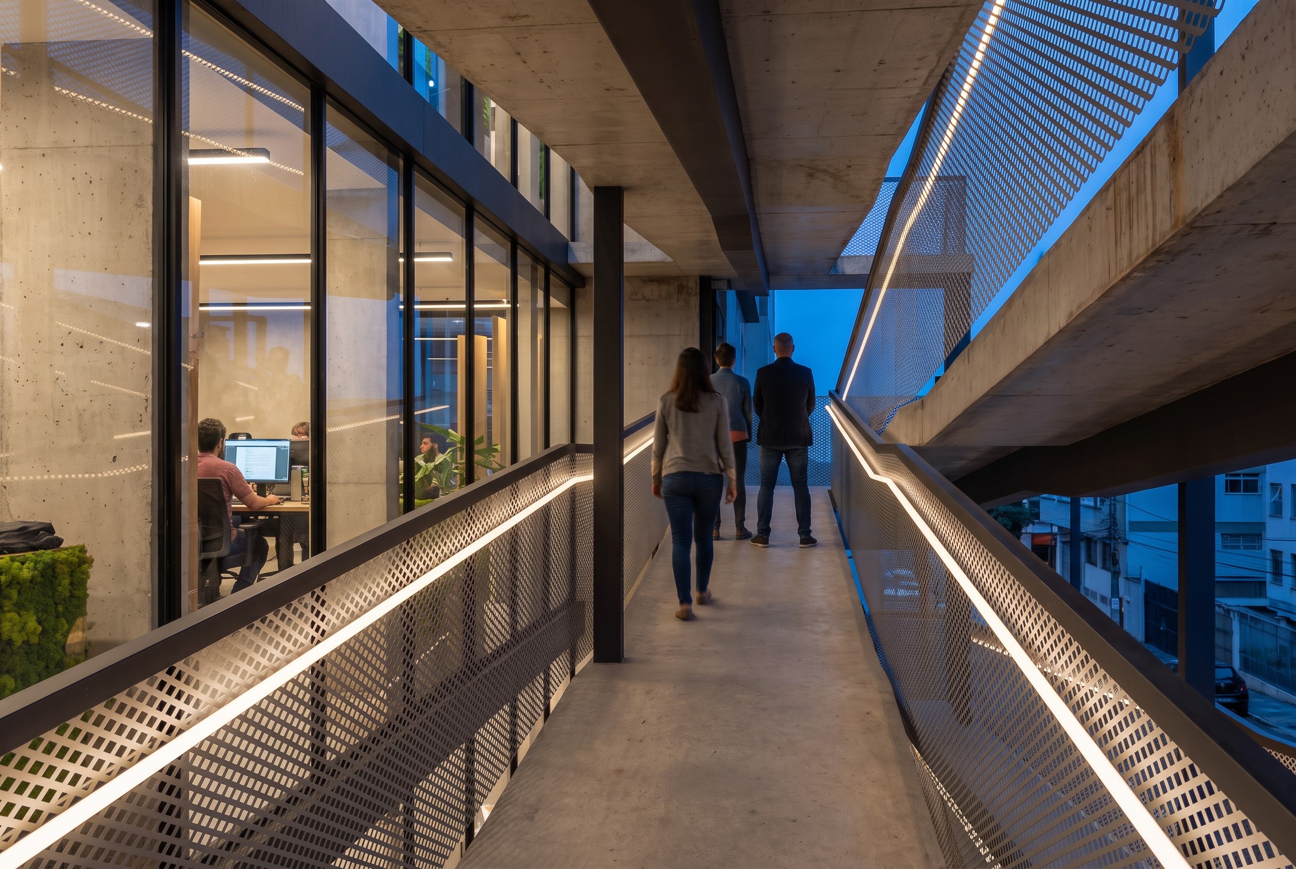 Walking up the ramp at dusk: expanded steel mesh guardrails with warm handrail light, the lit coworking behind the glass on the left