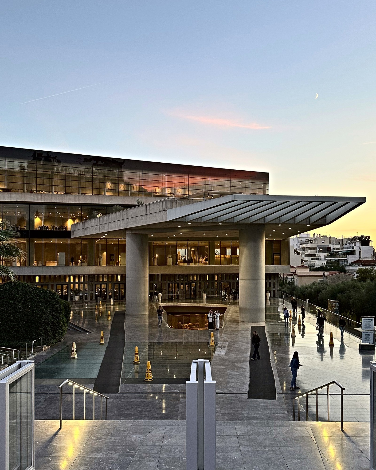 The Acropolis Museum at dusk, entrance canopy lit, glass floor over the excavation