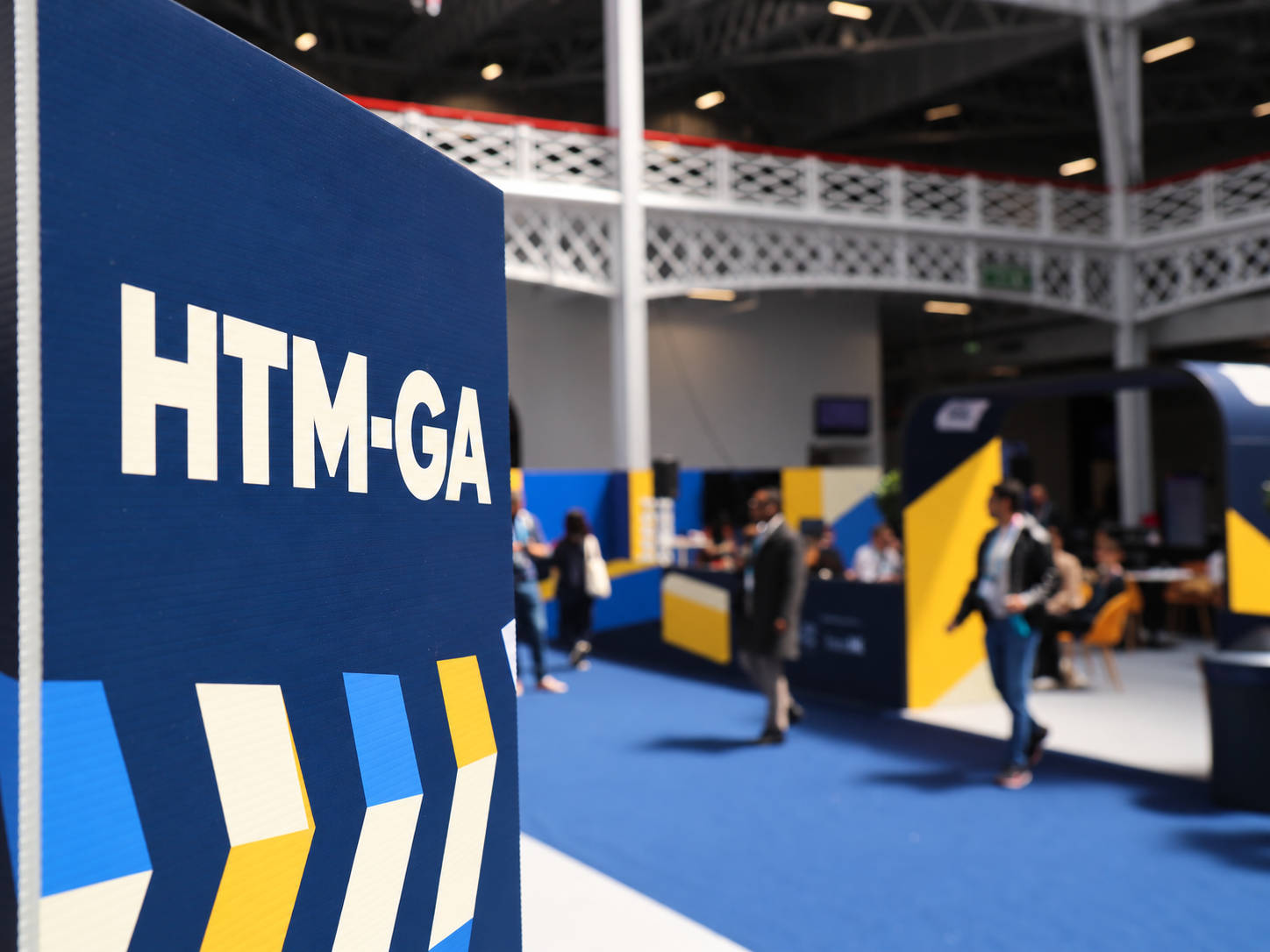 HTM-GA sign at a technology event with attendees in the background.