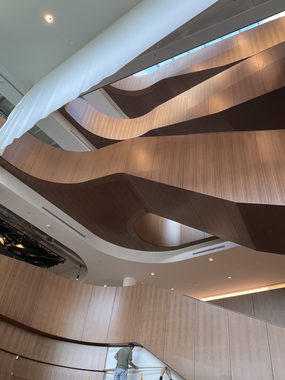 Interior shot showing a modern curved wooden staircase in a spacious building with a person at the bottom.