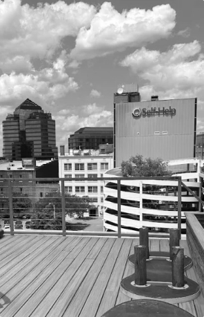 Cityscape with a wooden deck, railing, and buildings including one labeled Self Help under a cloudy sky.