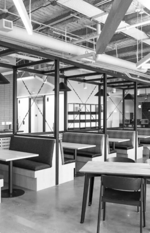 Empty modern cafeteria with booth seating, tables, chairs, and exposed ceiling pipes.