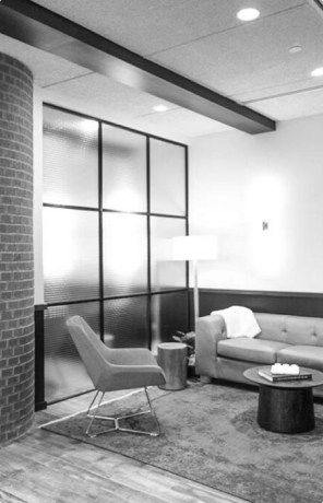 Modern living room with sofa, armchair, floor lamp, round coffee tables, and glass panel wall.