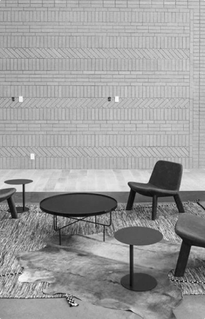Modern seating area with low chairs, round tables, layered rugs, and a textured brick wall.