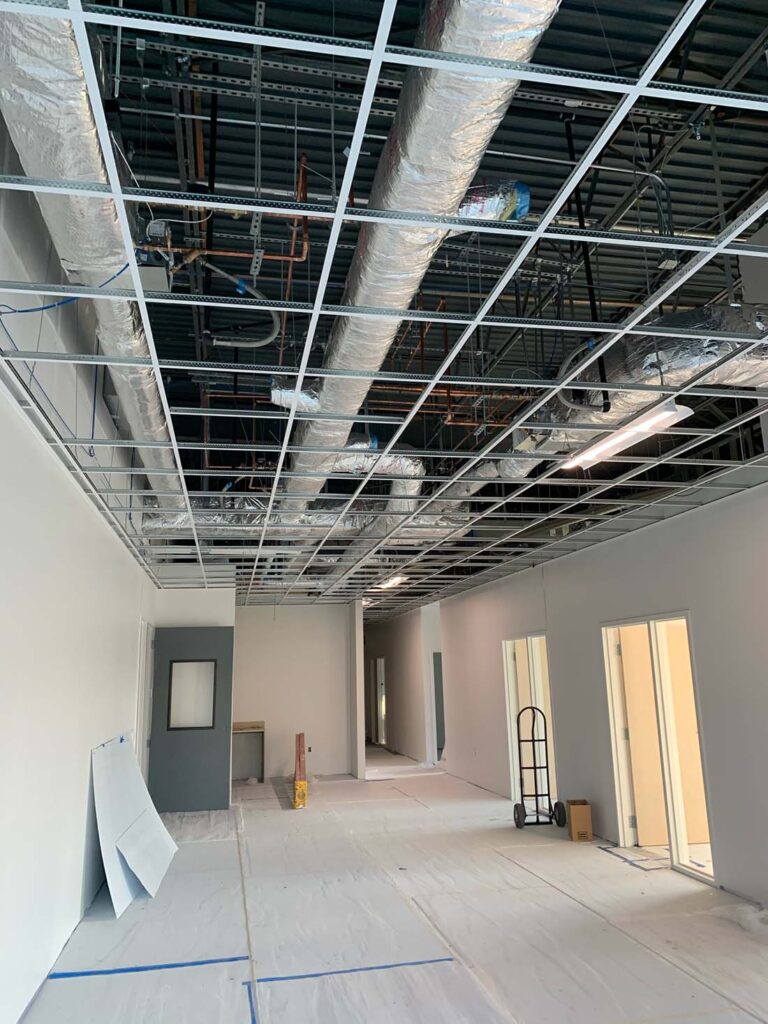 Interior view of a commercial space under construction with exposed ceiling ducts and white walls.