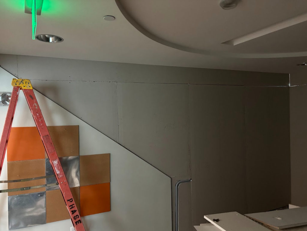 Interior wall under construction with red ladder and decorative square panels in orange and metal colors.