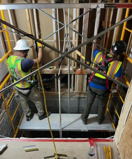 Two construction workers in safety gear working on scaffolding inside a building under construction.