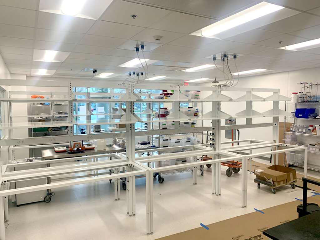 Empty white metal lab workbenches with shelves in a clean, bright laboratory room.