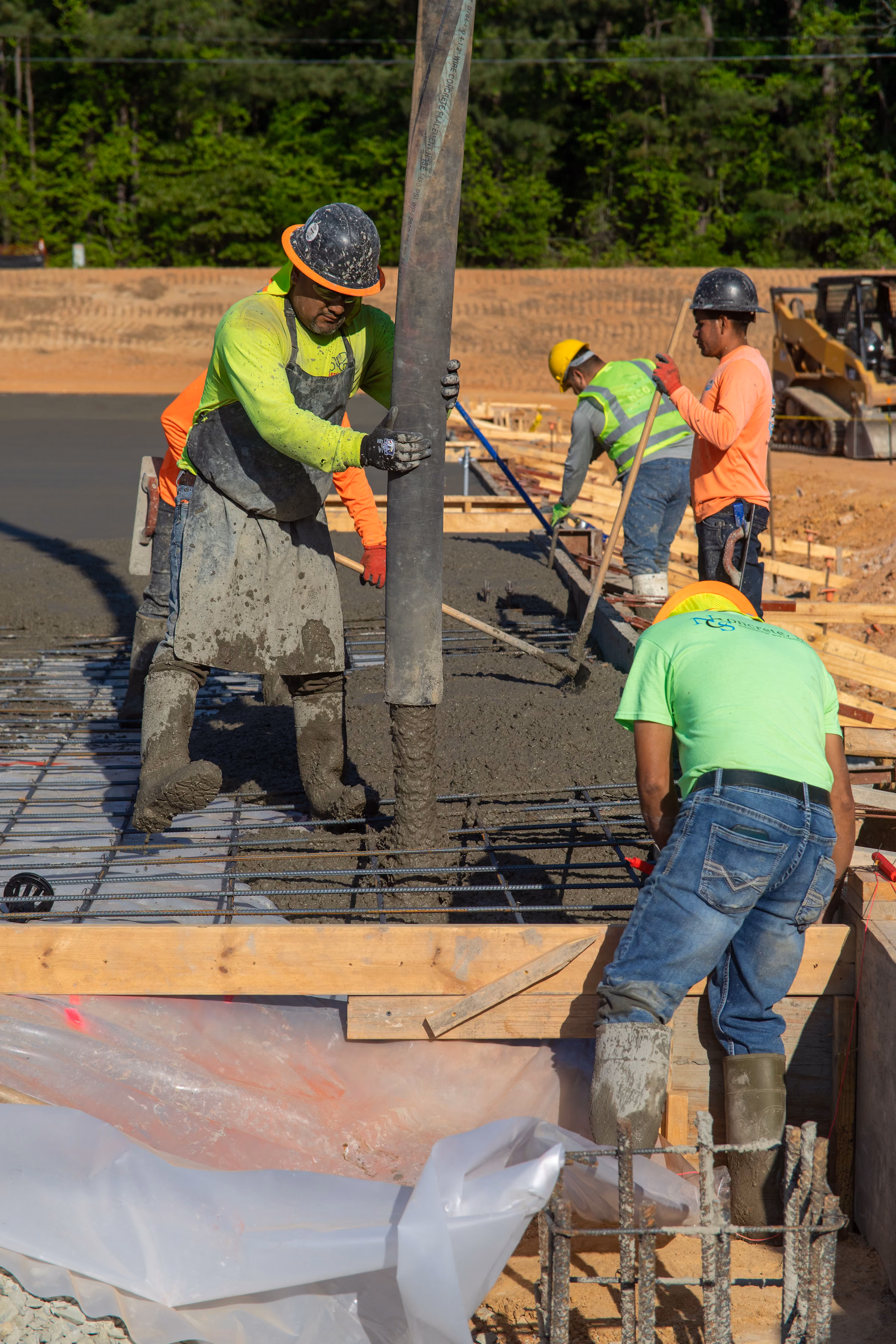 Construction workers pour and spread concrete over a steel rebar foundation at a construction site.