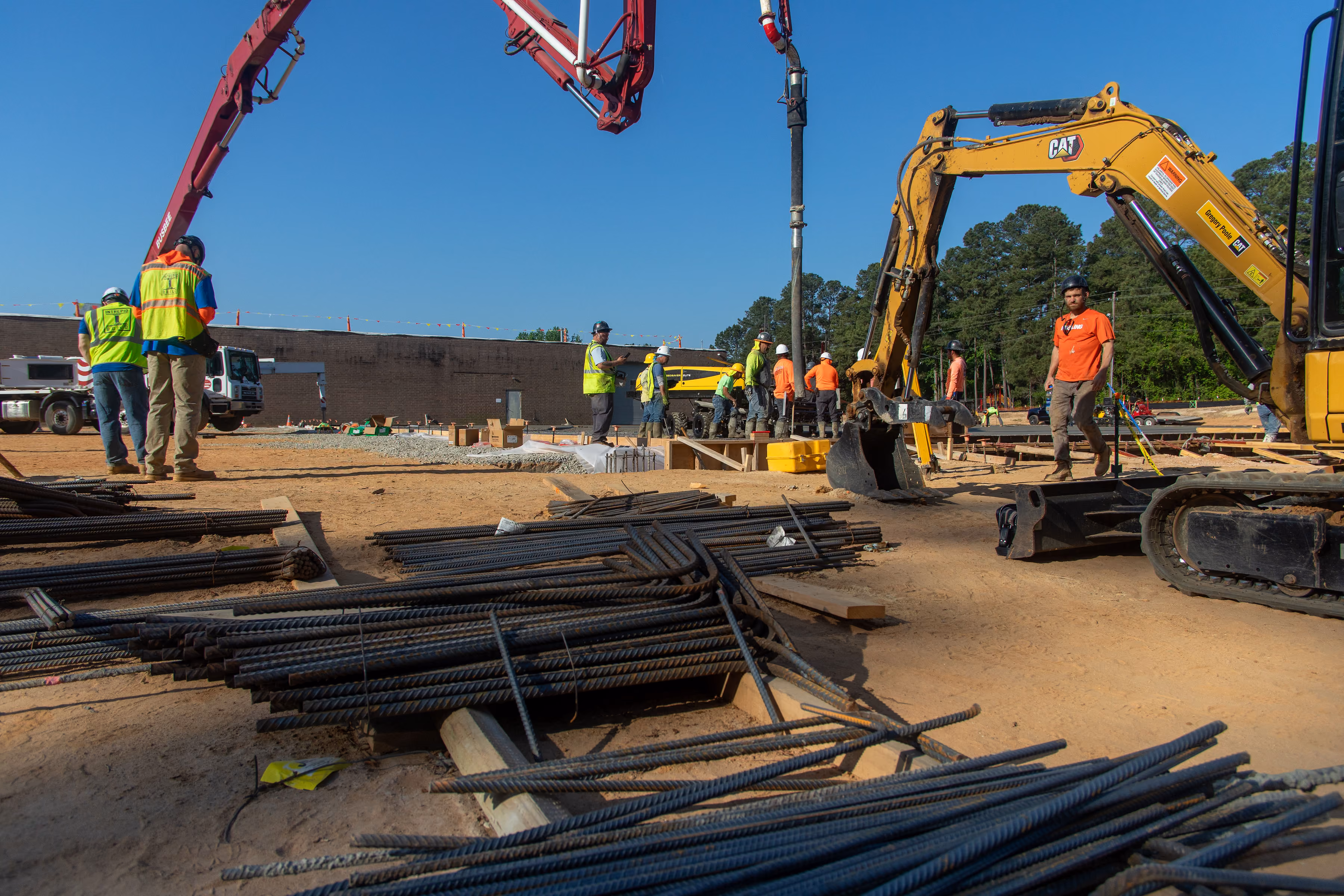 Construction site with workers in safety vests and helmets operating machinery and steel rods on ground.