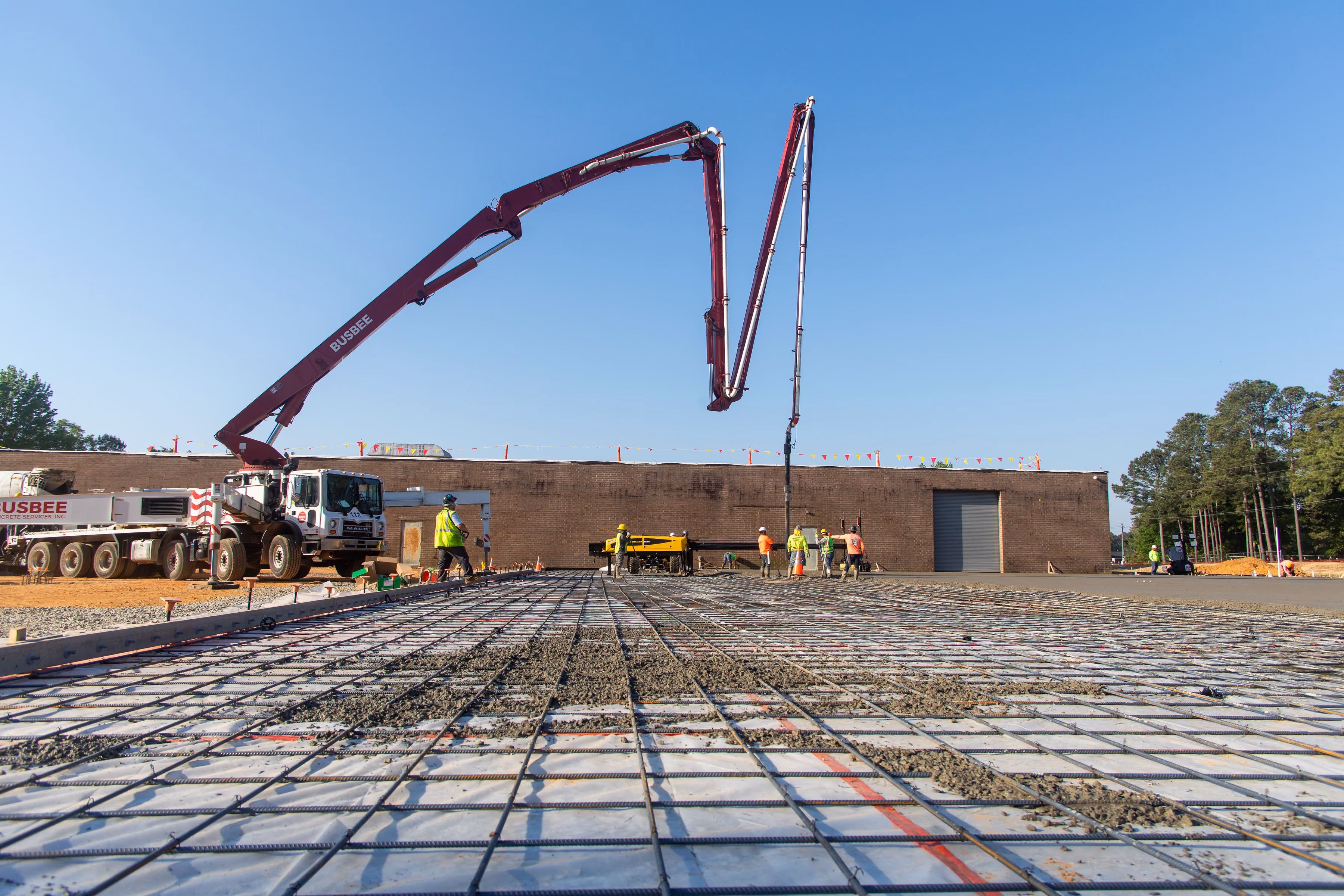 Construction workers pouring concrete on steel rebar at a building site using a large concrete pump truck.