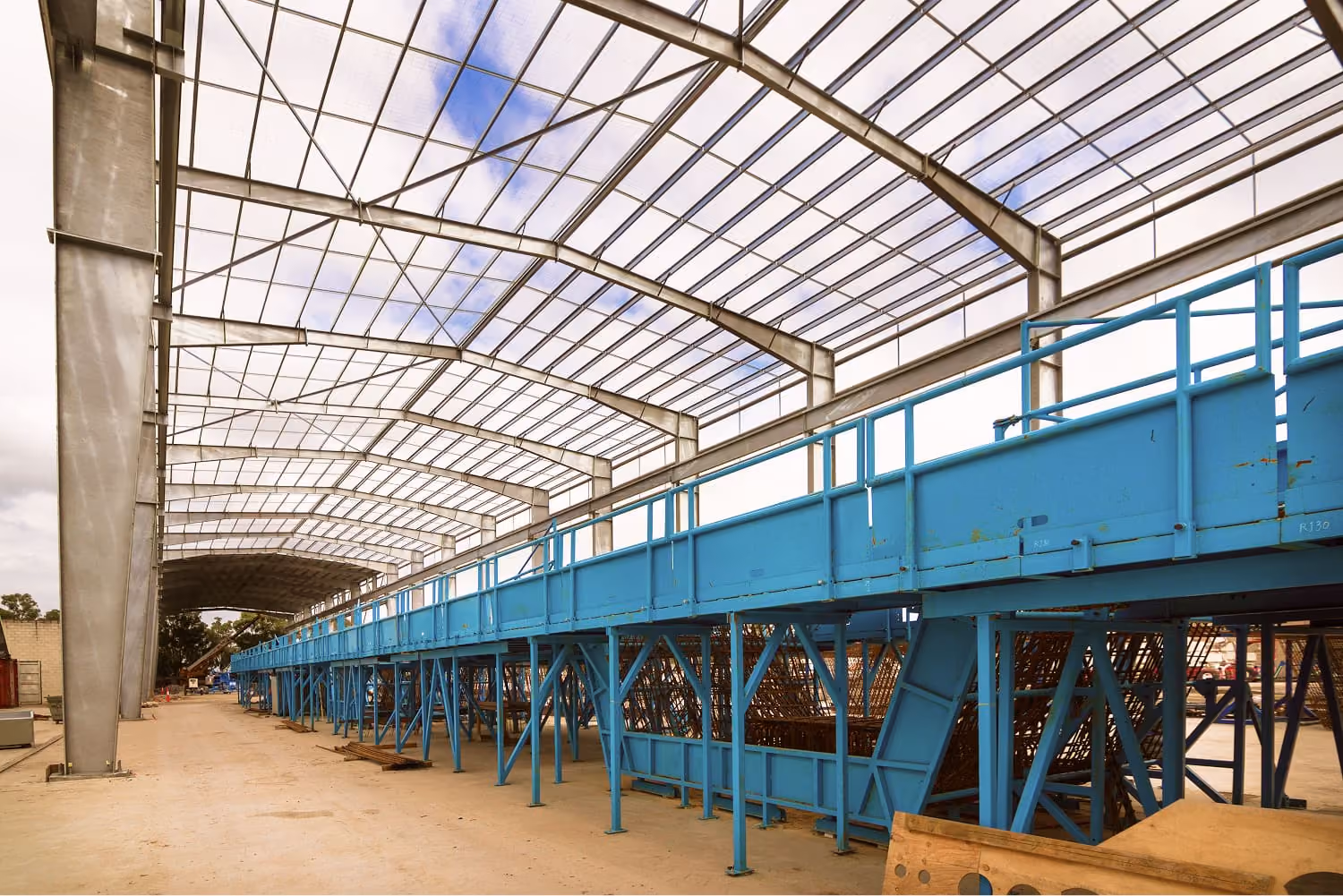 Blue steel conveyor structure under a curved translucent roof in an industrial building