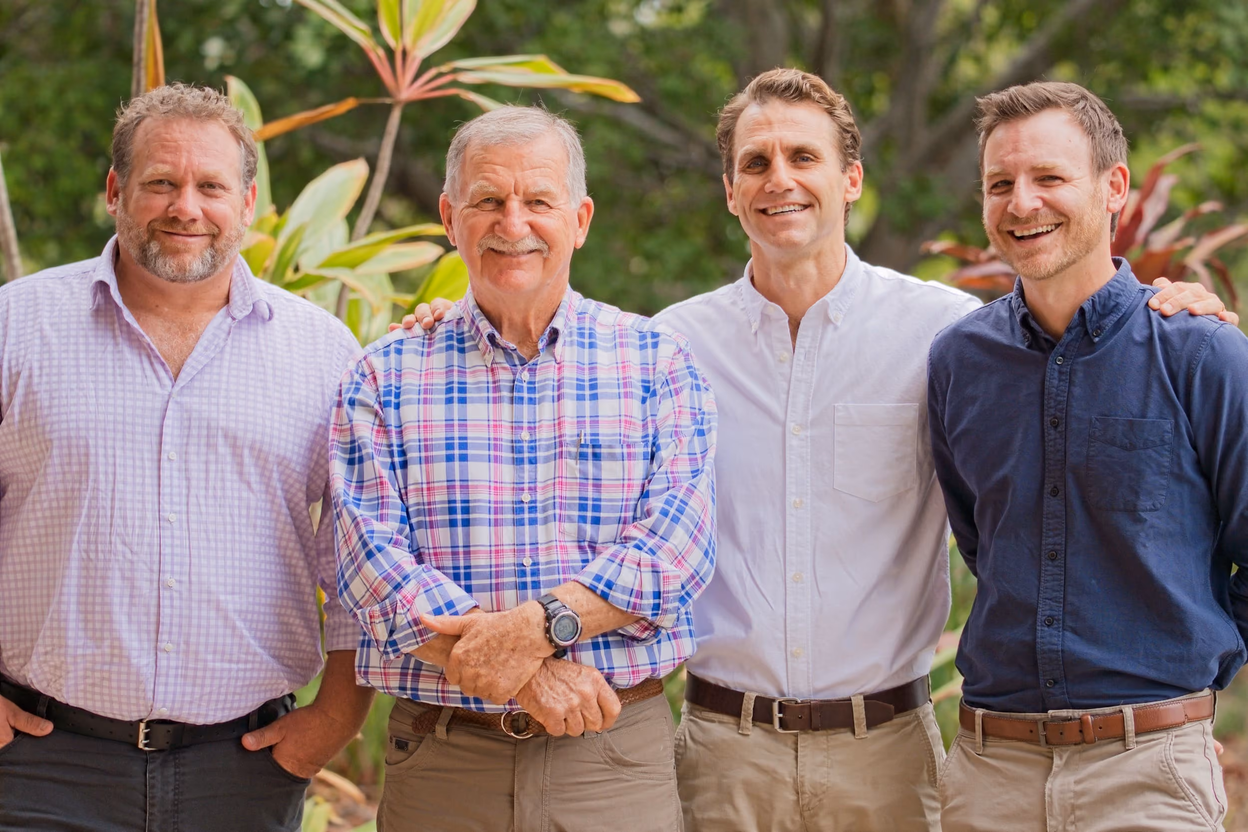 Four members of the DAKL team standing together outdoors in front of tropical greenery