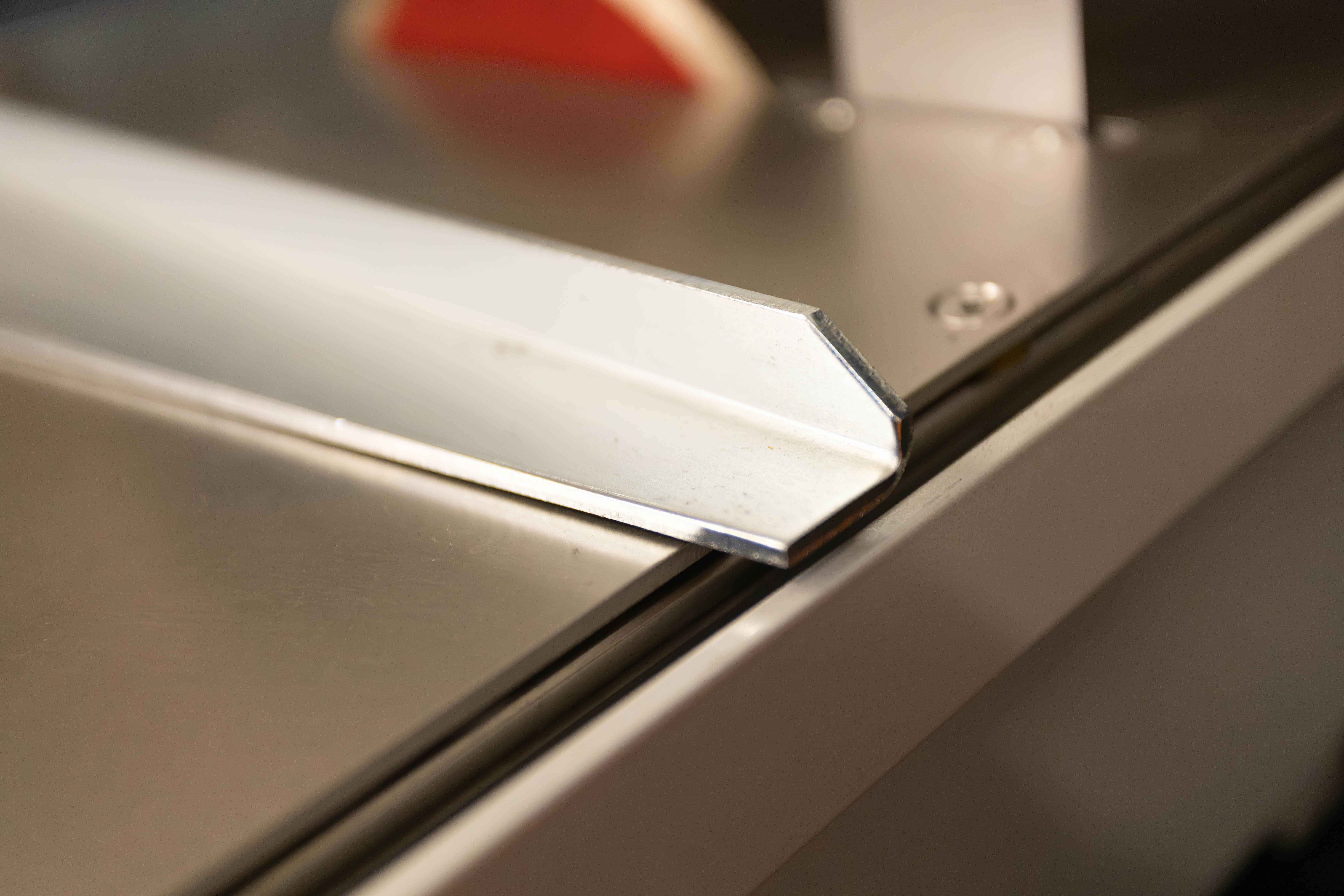 Nahaufnahme eines metallischen Winkels oder Kantenschutzes auf einer glatten Metalloberfläche mit verschwommenem Hintergrund.