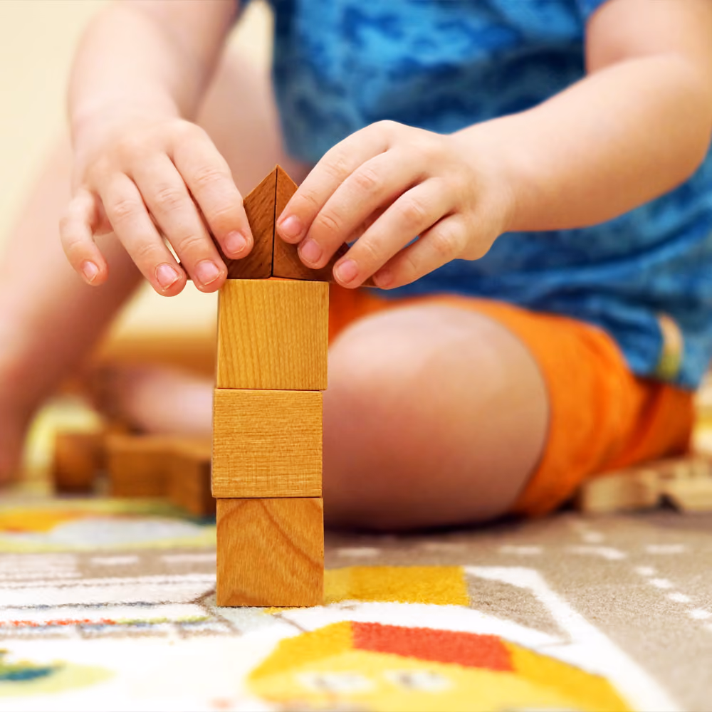 A child's hands stacking wooden blocks into a tower.
