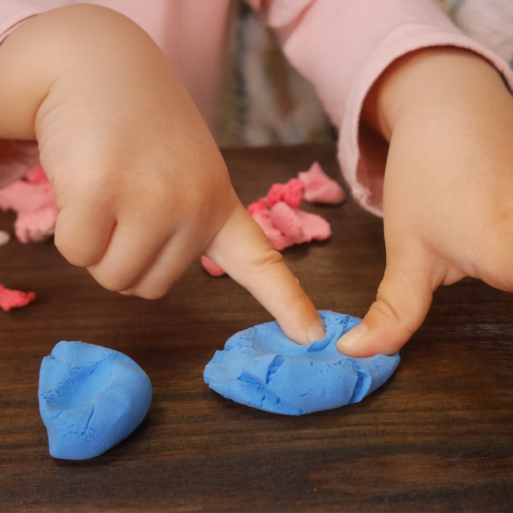 A child pressing shapes into pink playdough at the craft table.