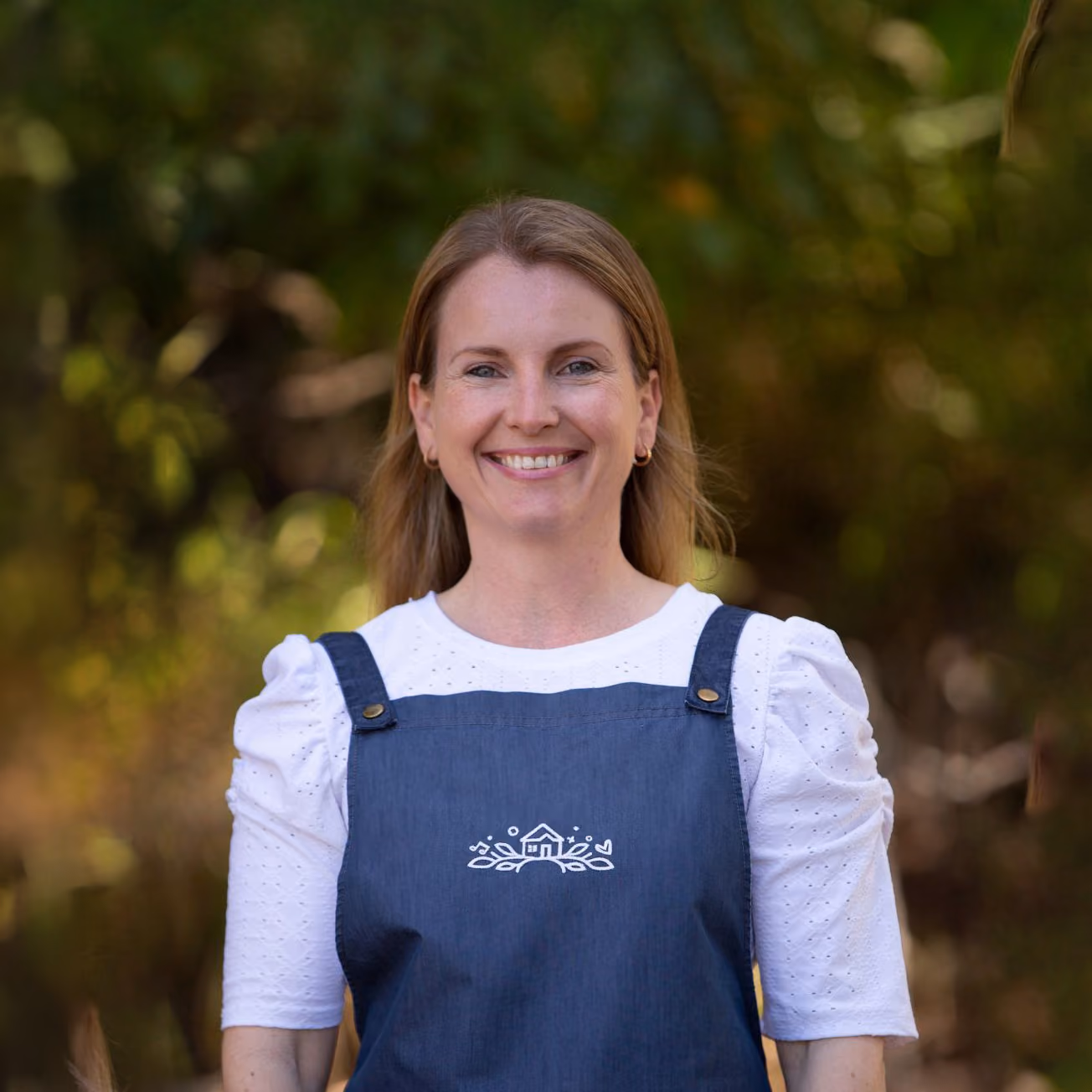 An educator at Kindy Cottage Sandgate smiling outdoors in a denim apron.