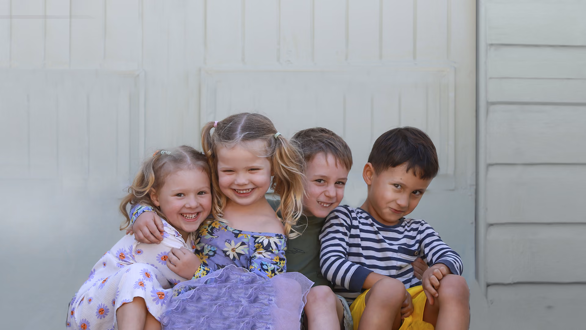Four children sitting together on the cottage verandah, smiling.