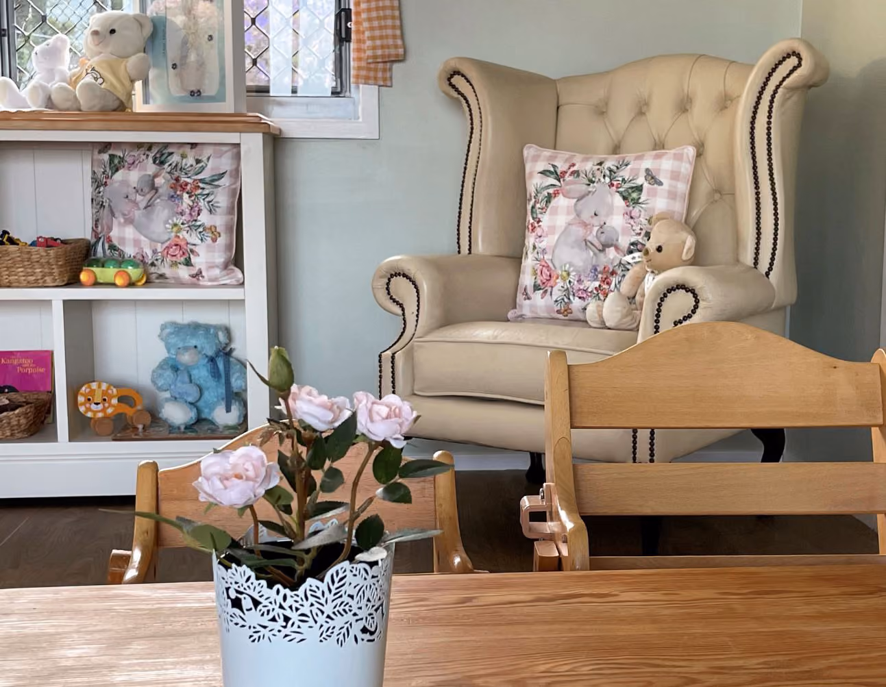 A cosy cottage corner with a floral armchair, shelves of soft toys and fresh roses.